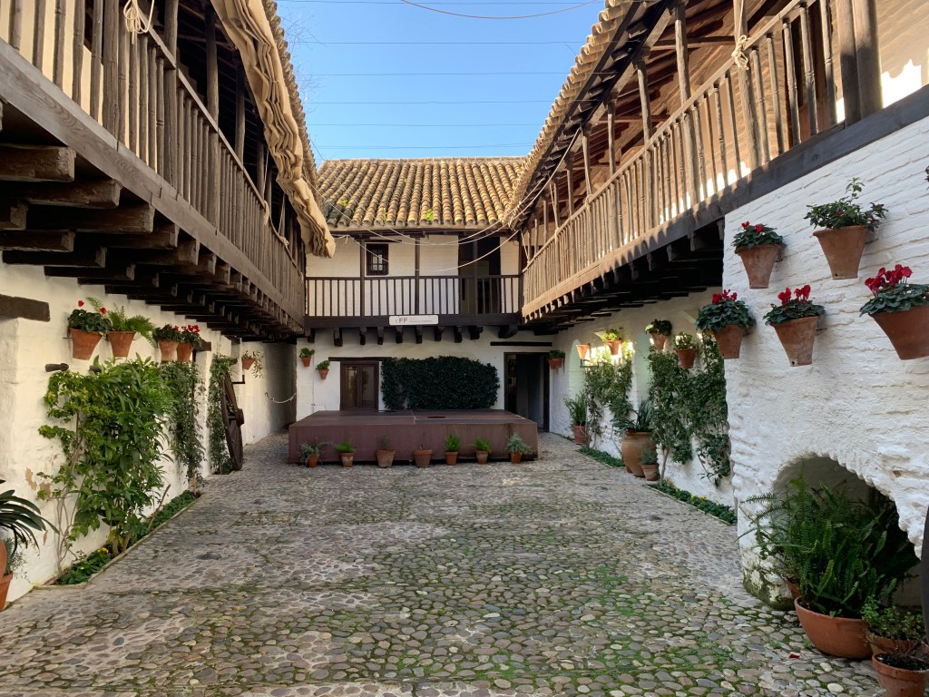 Courtyard with hanging pots of geraniums, tiled roof and wooden ballustrades.