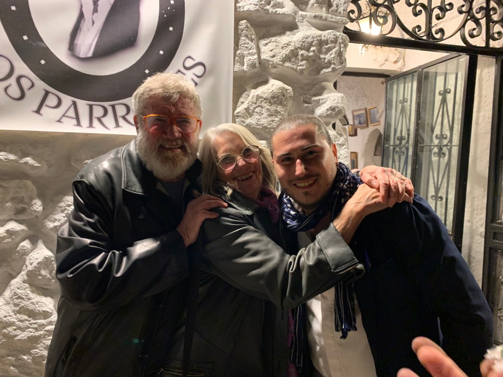 Man, woman, and man hugging outside a white stone stone wall