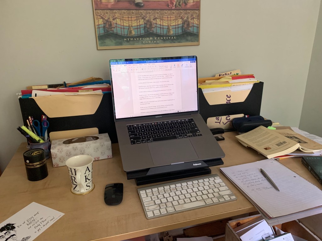 An open computer, books, tea cup, files. A desktop.