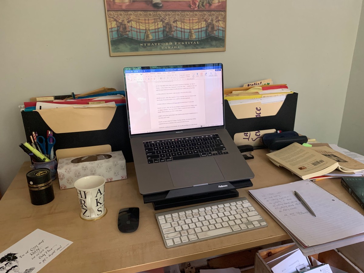 a desk with open computer, books, files and teacup.